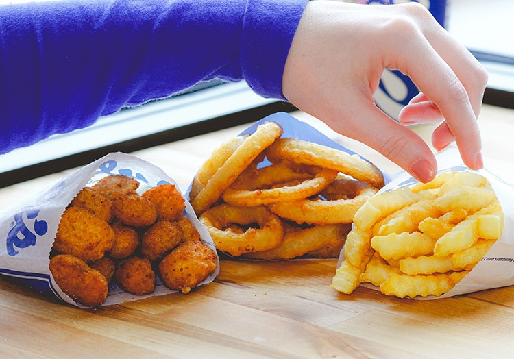 Link to story: Can we guess which side you're craving? A hand reaches for Onion Rings, Crinkle Cut Fries and Cheese Curds on a table. 