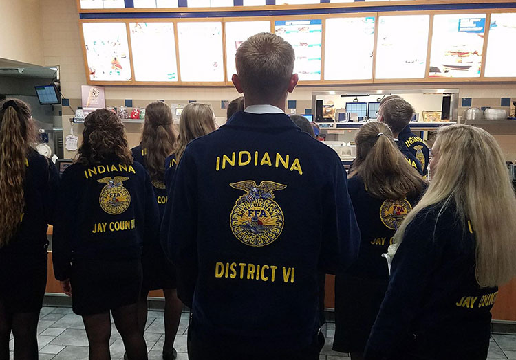 Link to story: Meet Culver's Team Members active in FFA. Photo of FFA members in their blue jackets stand in a Culver’s restaurant looking at the menu board.