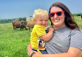 Link to story: Celebrating Women in Agriculture. Carrie Mess holds her son while standing near her cows in a field.