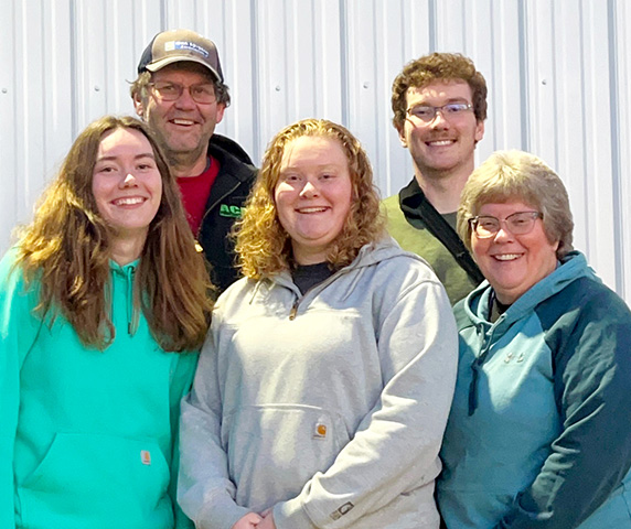 Family of five standing in front of a wall, smiling. 