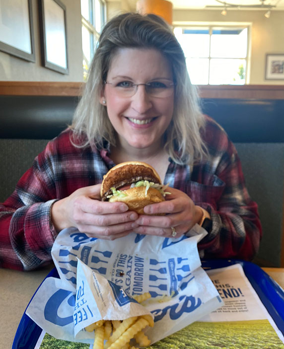 A woman smiles while holding a CurderBurger.